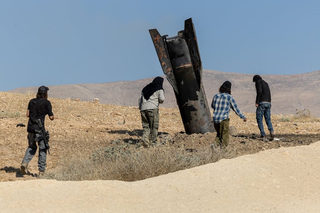 Israeli settlers in the West Bank next to part of a missile protruding from the ground, following strikes from Iran. Photo: Reuters Israeli settlers in the West Bank next to part of a missile protruding from the ground, following strikes from Iran. Photo: Reuters