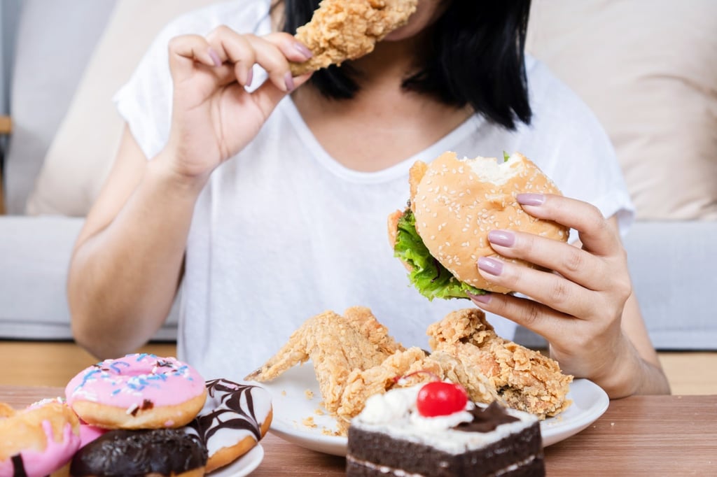 A woman binge eating a burger, fried chicken, doughnuts and other desserts. Photo: Shutterstock A woman binge eating a burger, fried chicken, doughnuts and other desserts. Photo: Shutterstock