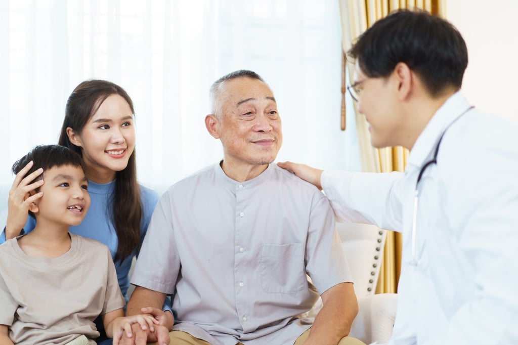 A male doctor chats to an elderly man during a health check-up as he sits with two family members. Photo: Shutterstock