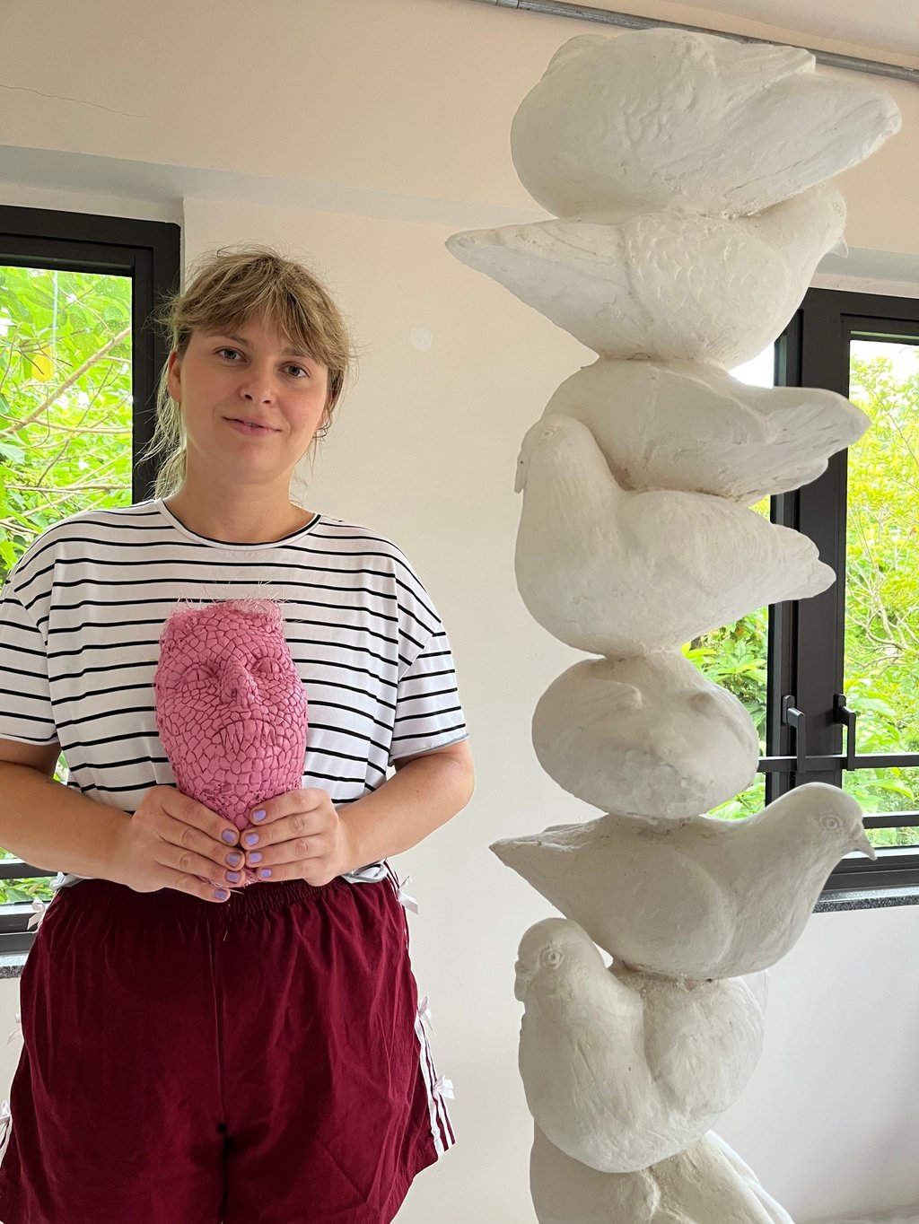 Nikola Emma Rysava holds a resin mask of her face, patterned to look like snake skin, beside a plaster column of pigeons, at her residency at Ma Wan 1868. Photo: Enid Tsui