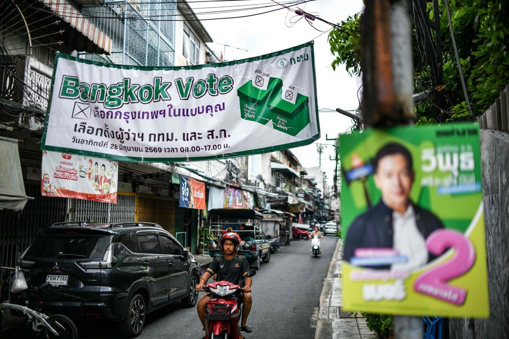 A man rides his motorbike under a banner displayed ahead of the Bangkok gubernatorial election on June 4. Photo: AFP