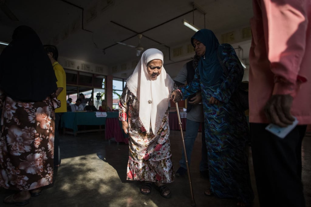 An elderly Malaysian woman is helped as she leaves after casting her vote at a polling station during the 14th general election in Alor Setar in 2018. Photo: AFP An elderly Malaysian woman is helped as she leaves after casting her vote at a polling station during the 14th general election in Alor Setar in 2018. Photo: AFP