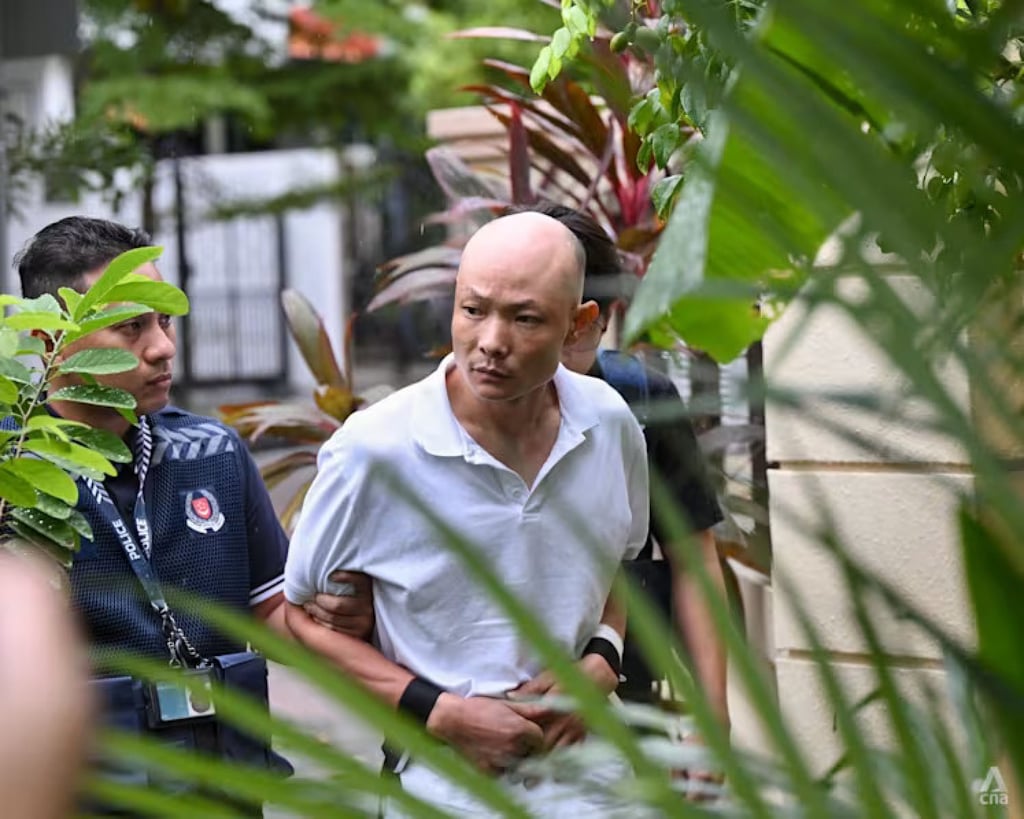 Huang Xiaozong being escorted by police officers along residential units in Serangoon in December 2025. Photo: CNA