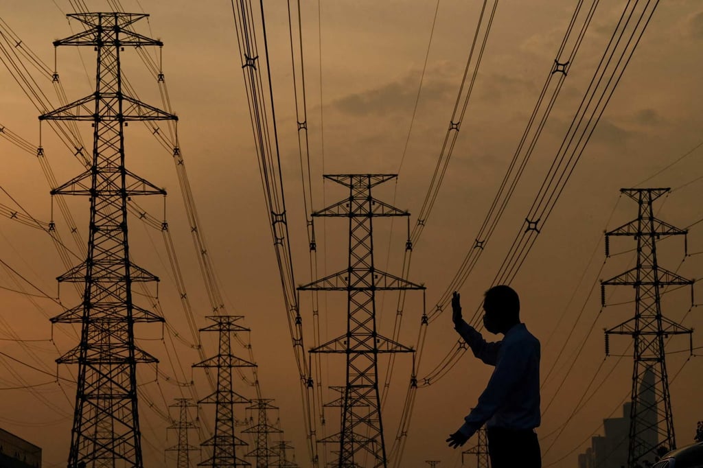 A parking assistant at work below power lines in Beijing. In China, local governments are increasingly deploying private capital to speed the buildout of necessary power infrastructure. Photo: AFP