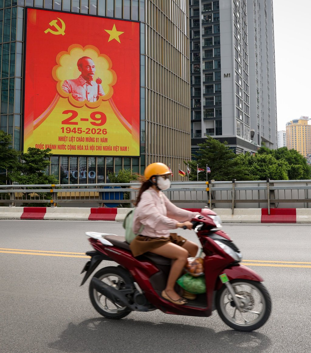 A young woman rides past a hoarding for the coming 81st National Day anniversary in Hanoi on Monday. Photo: EPA