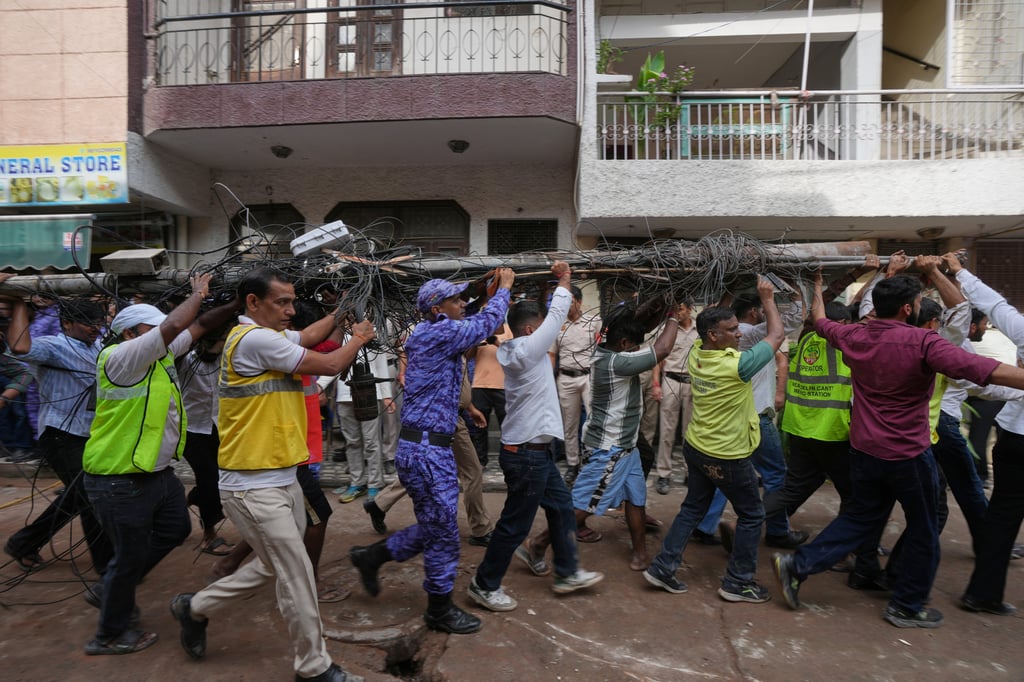 Rescue workers carry an electric pole near the site of a collapsed building in New Delhi on Sunday. Photo: AP