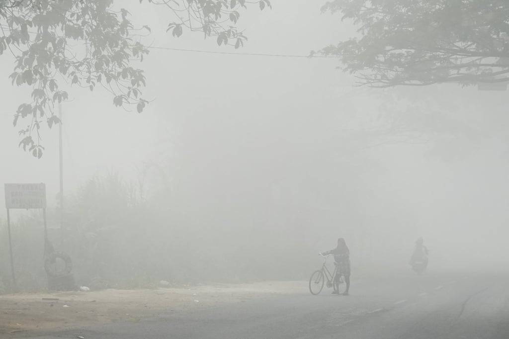 A person walks with a bicycle along a road shrouded in haze from wildfires in Banyuasin, South Sumatra province, Indonesia, on Sunday. Photo: Reuters