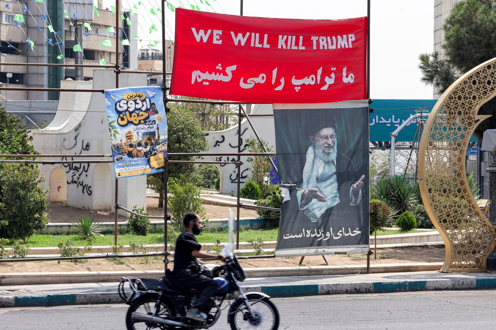 A man rides a motorcycle near a banner bearing a message in English and Persian reading “We will kill Trump” in Tehran on Wednesday. Photo: TNS