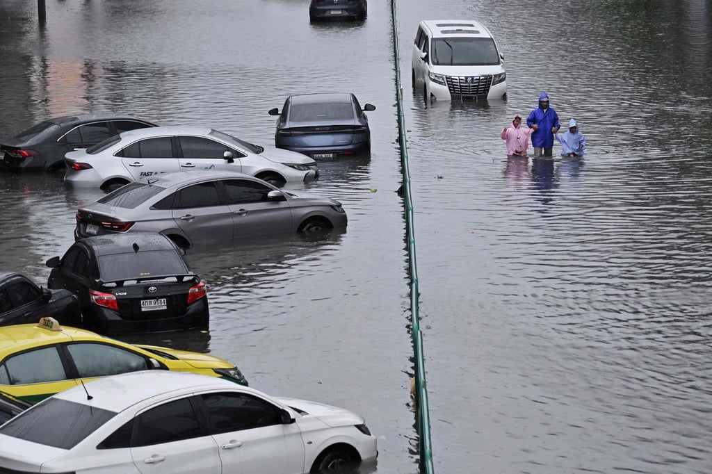 People walk past abandoned vehicles on a flooded Petchaburi Road in Bangkok on Saturday. Photo: AFP People walk past abandoned vehicles on a flooded Petchaburi Road in Bangkok on Saturday. Photo: AFP