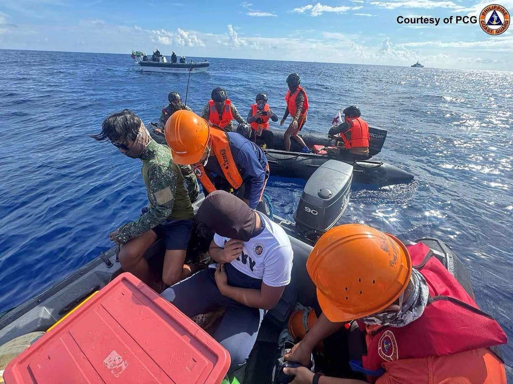Chinese coastguard personnel (background) watch Philippine Navy members (back centre) transfer a colleague during a medical evacuation near Second Thomas Shoal on October 8. Photo: Philippines Coast Guard / AFP