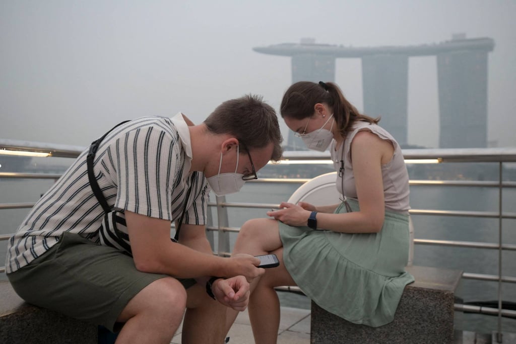 Tourists wear protective masks while seated across Marina Bay Sands in Singapore on Thursday. Photo: AFP Tourists wear protective masks while seated across Marina Bay Sands in Singapore on Thursday. Photo: AFP