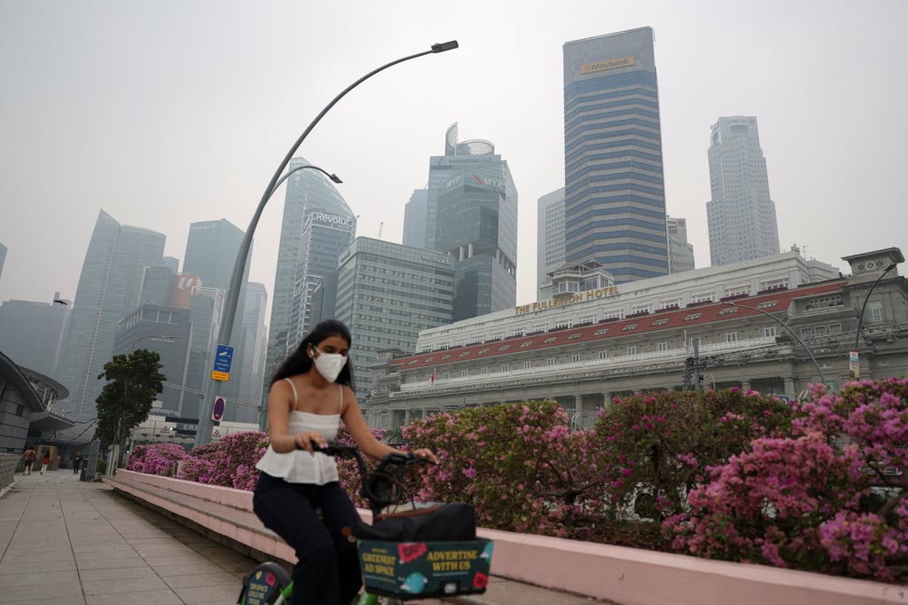 A woman in a face mask rides a bicycle through Singapore’s haze-covered central business district on Friday. Photo: Reuters