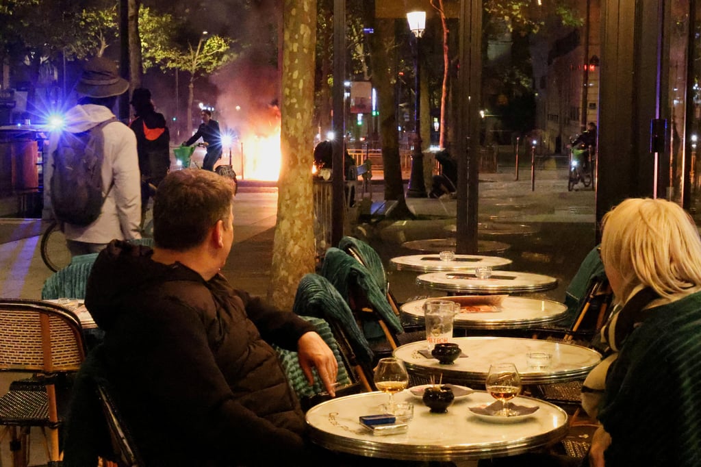 Customers at a cafe watch a fire set by rioters in Paris on Saturday. Photo: Reuters