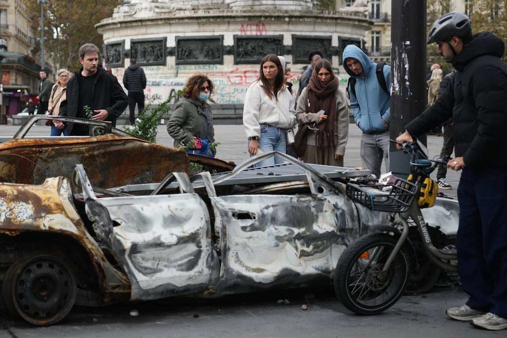 People watch a burnt-out car in Paris on Tuesday. Photo: AP