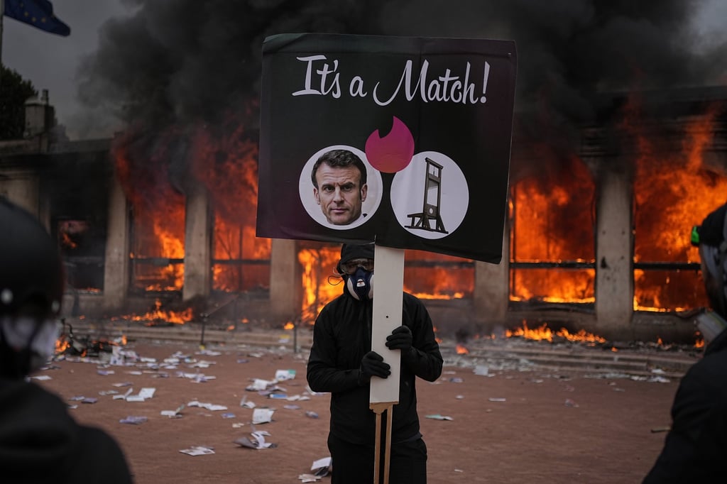 A protester holds a placard with a photo of French President Emmanuel Macron and a guillotine in front of a burning tourism in Lyon on Saturday. Photo: AP
