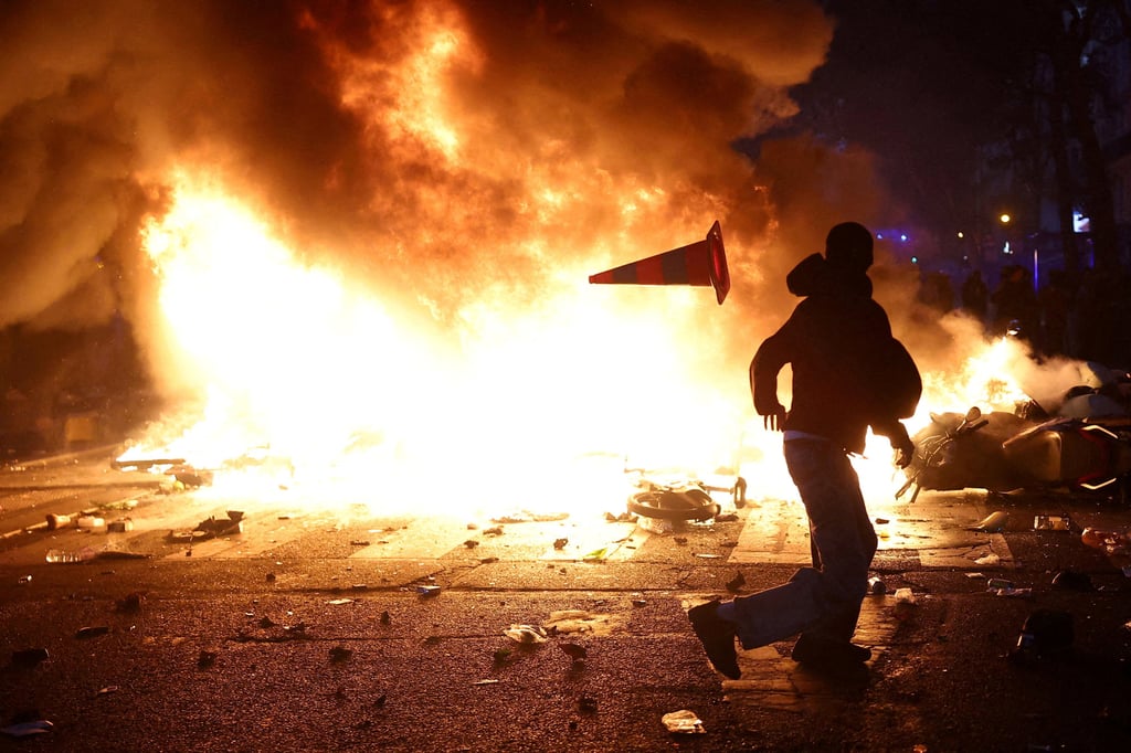 A man throws a plastic traffic cone through a burning barricade amid clashes during a protest against the cost of living in Paris on Saturday. Photo: Reuters