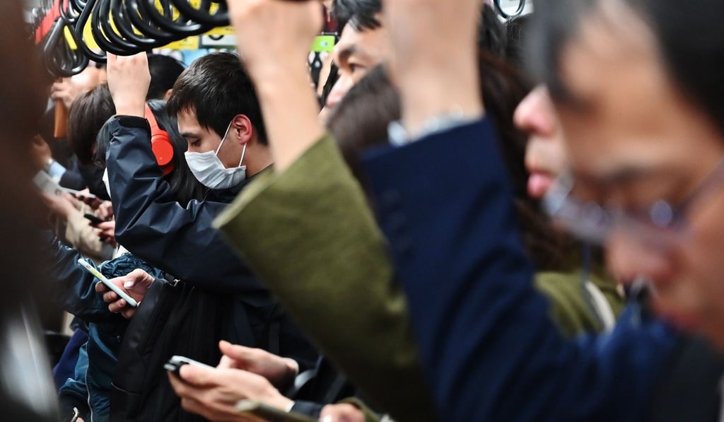 Commuters use their mobile phones while travelling on a coach of the Tokyo Metro network in Tokyo. Photo by Charly Triballeau / AFP)