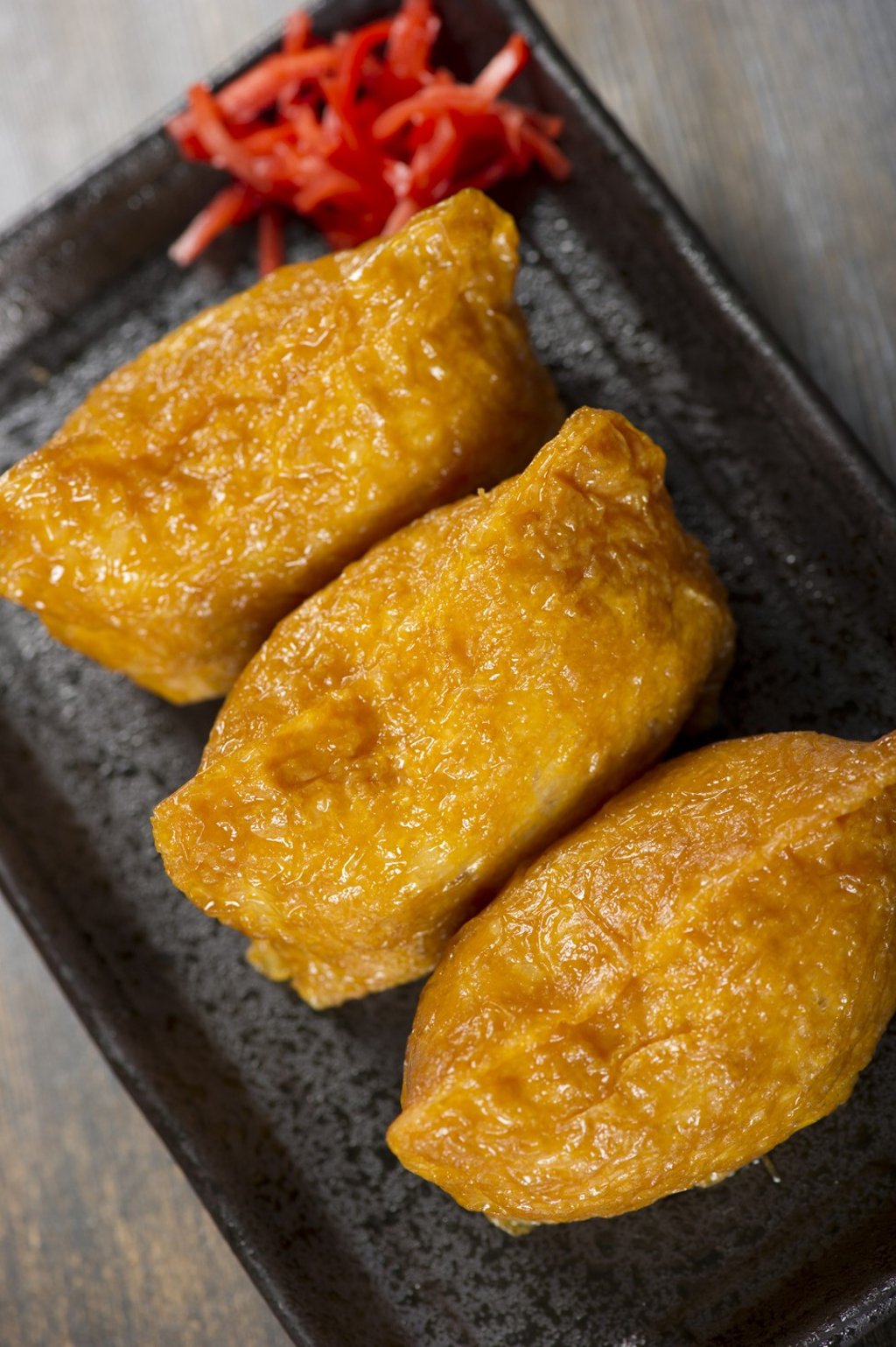 Japanese Inari sushi consists of a pouch of fried tofu skin filled with sushi rice, with pickled ginger on the side.