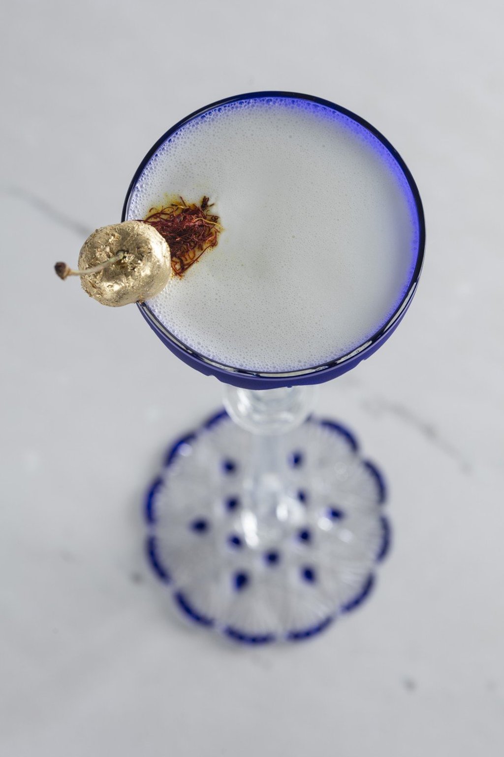 The cocktail is garnished with an Amarena cherry hand-pressed with gold leaf set atop saffron.