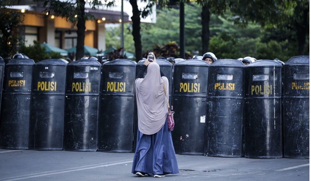 A woman takes pictures of riot police guarding Indonesia’s Election Supervisory Agency. Photo: EPA