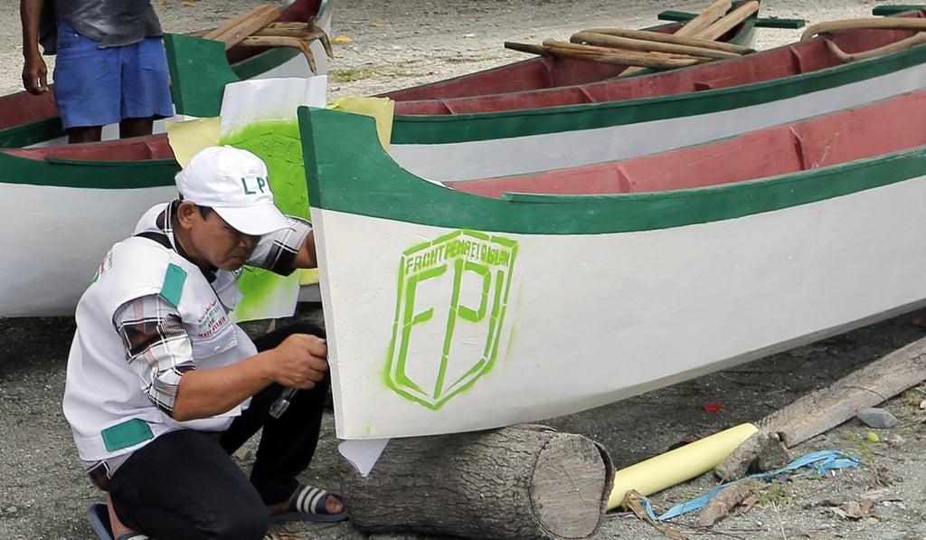 A member of the Islamic Defenders Front paints the group's logo on a boat donated to fishermen affected by the 2018 tsunami in Palu. Photo: AP