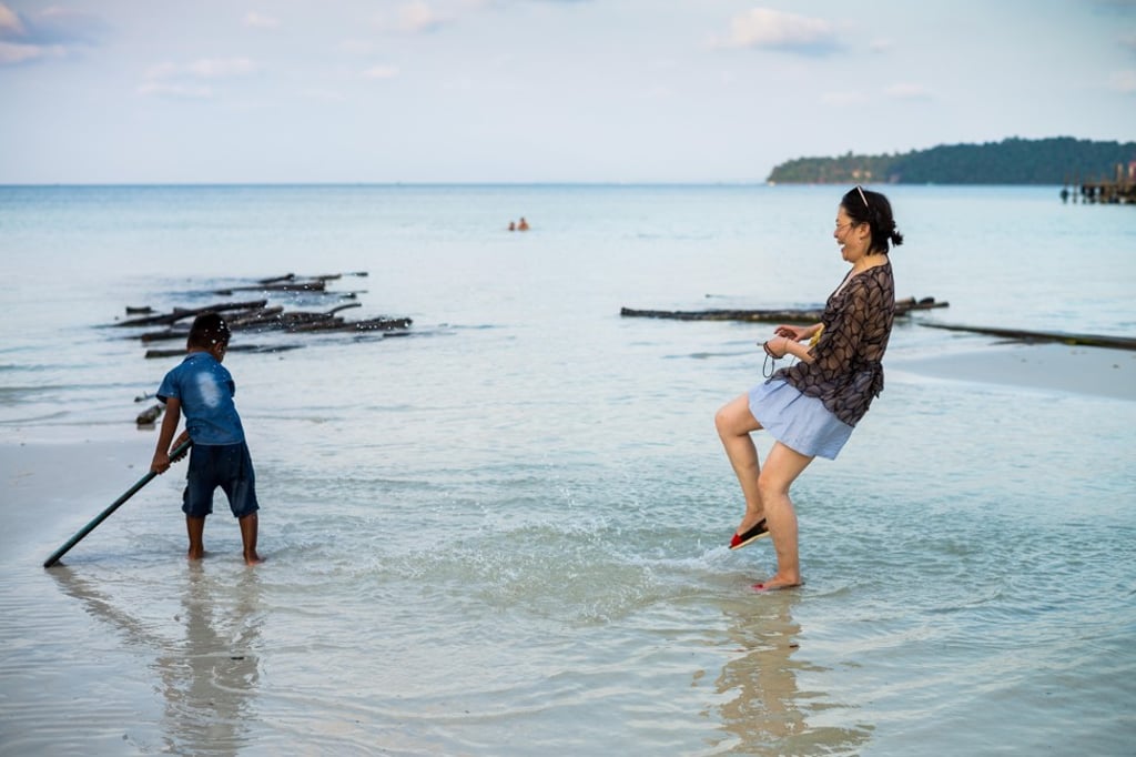 An Asian tourist in Cambodia playing with a local boy on the beach. Interacting with local people and communities is one of the keys to a memorable travel experience, according to a new report. Photo: Alamy