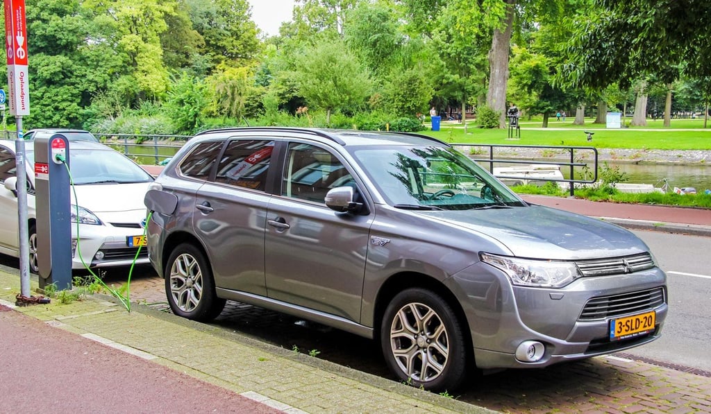 A Mitsubishi Outlander PHEV, which can rely on an engine and fuel power, recharges at a city street charging station.