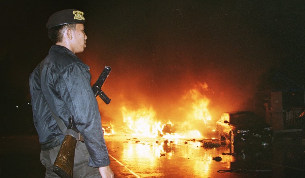 An Indonesian policeman watches as cars burn in the street following bomb explosions in front of a church in Jakarta on December 24, 2000. Photo: AP