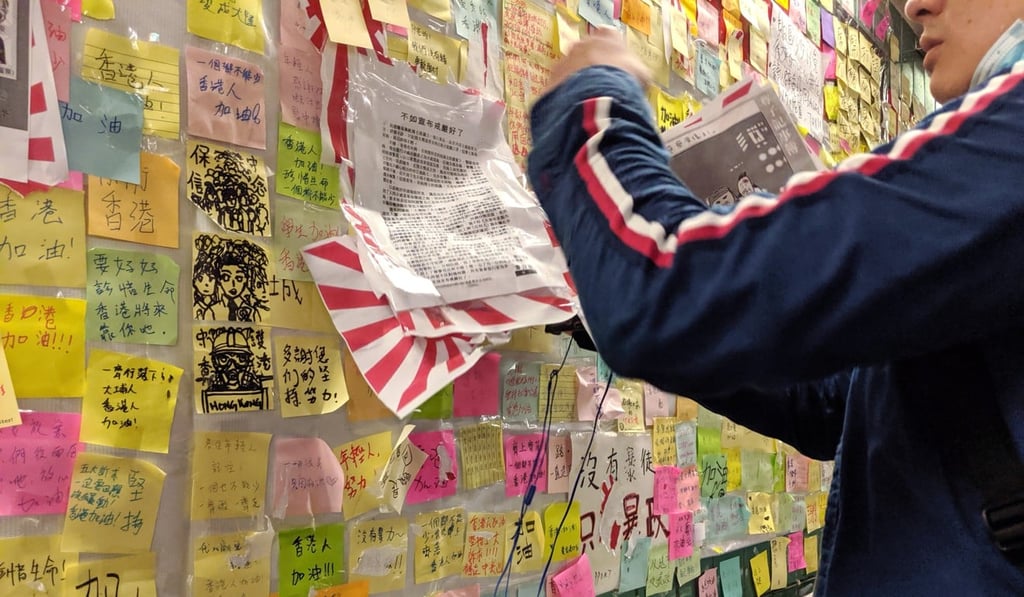 A volunteer removes a rising sun flag from Tai Po’s Lennon Wall. Photo: Sum Lok-kei