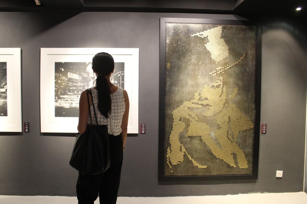 A visitor views Simon Wan’s photography (left) and a Giraffe Leung artwork made from coins at La Galerie Paris 1839. Photo: Snow Xia