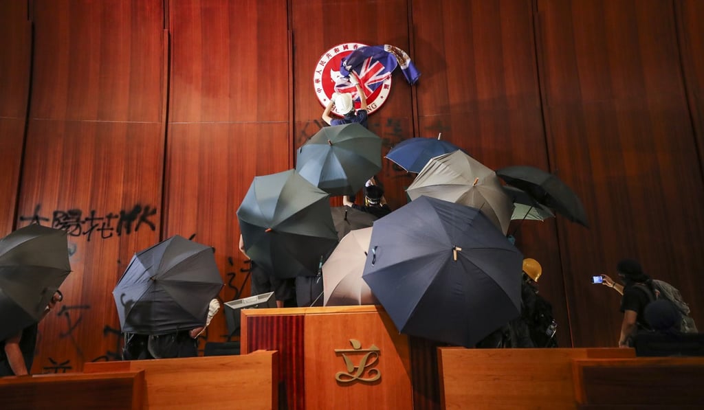 A protester covers the Hong Kong Special Administrative Region emblem with a British colonial flag as protesters storm the Legislative Council chamber in Tamar on July 1. Photo: Sam Tsang