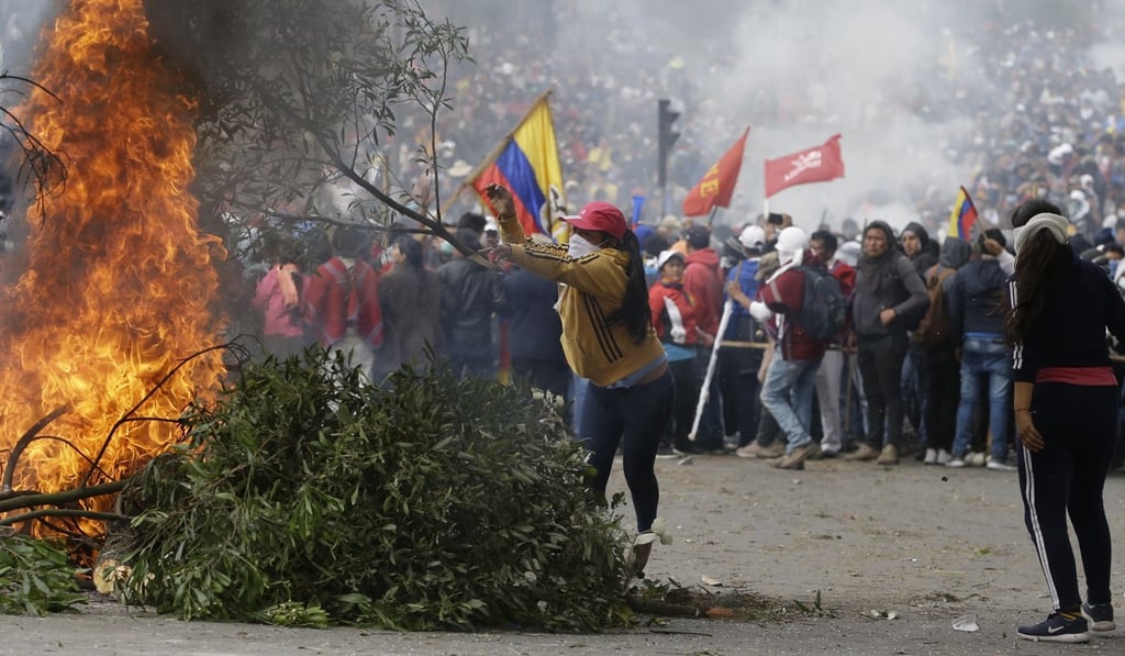 An anti-government demonstrator adds a branch to a burning barricade during a protest in Quito on Tuesday. Photo: AP An anti-government demonstrator adds a branch to a burning barricade during a protest in Quito on Tuesday. Photo: AP