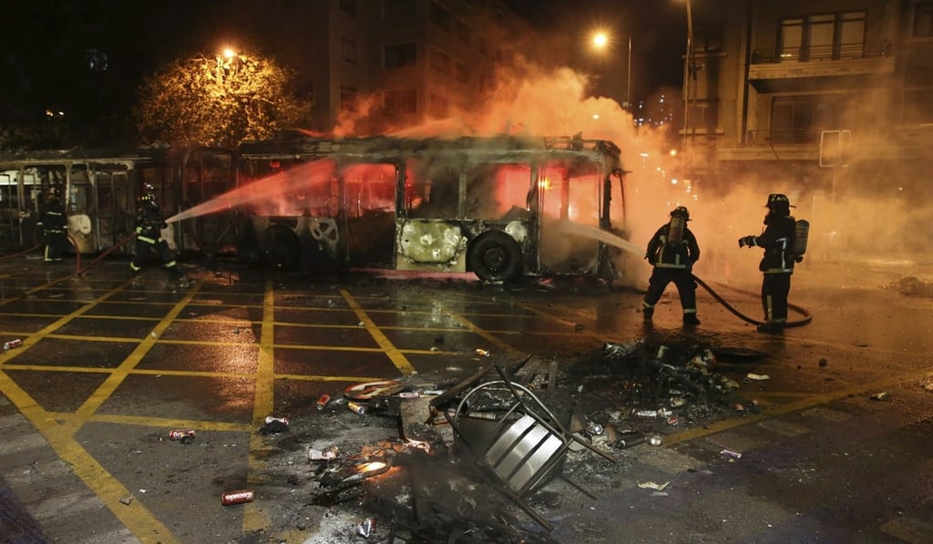Firefighters put out the flames on a burning bus during a protest in Santiago. Photo: AP Firefighters put out the flames on a burning bus during a protest in Santiago. Photo: AP