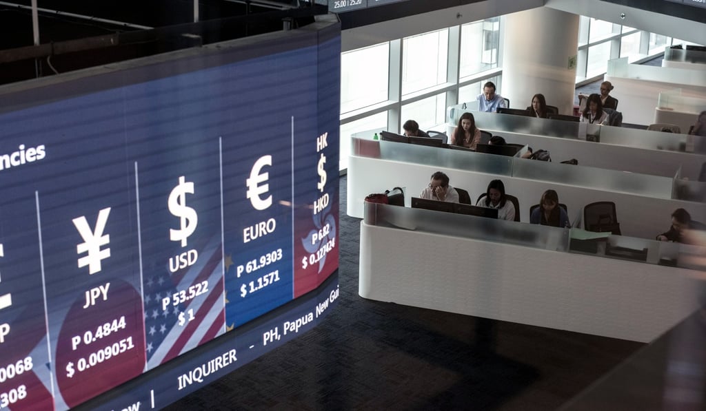 Traders work beneath a monitor displaying foreign exchange rates on the trading floor of the Philippine Stock Exchange. Photo: Bloomberg