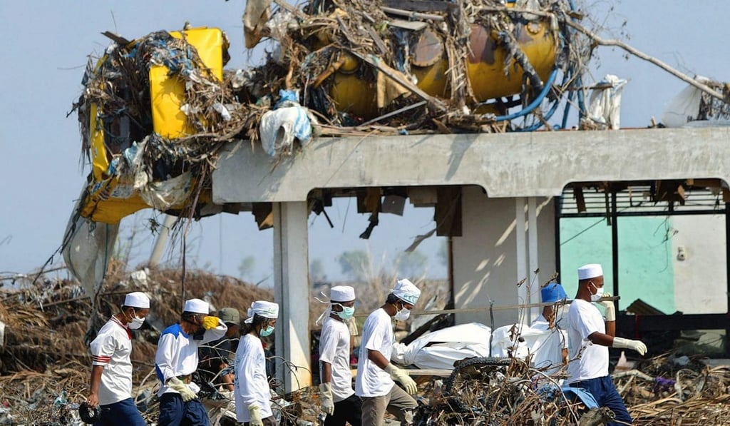 Volunteers carry a body as they walk past a truck destroyed by the tsunami in Banda Aceh, Indonesia, on January 22, 2005. Photo: EPA