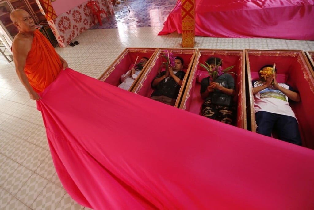 Monks cover worshippers as they take turns lying in coffins at a temple in suburban Bangkok. Photo: AP