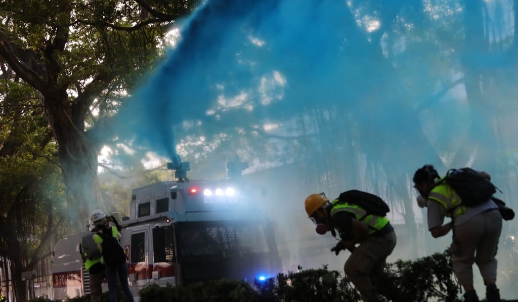Journalists duck as police fire a water cannon at anti-government protesters. Photo: May Tse