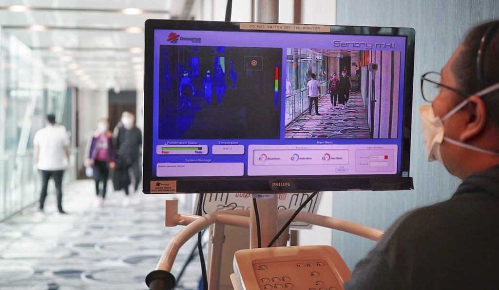 A staff member at Changi Airport screens the body temperatures of arriving passengers. Photo: EPA