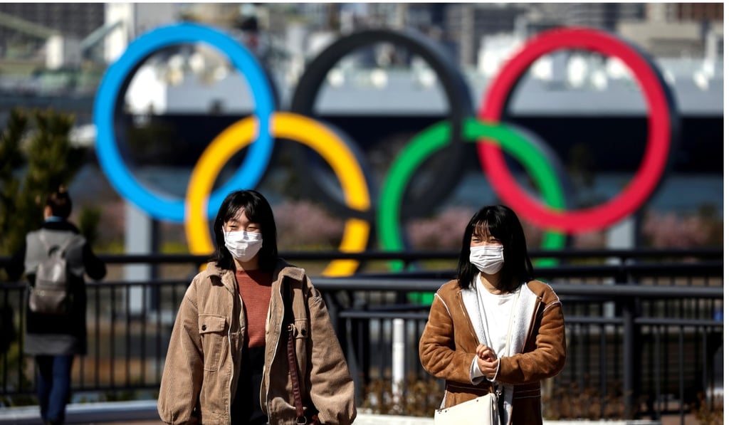 People wearing protective face masks are seen in front of the Olympic rings at the waterfront area at Odaiba Marine Park in Tokyo, Japan. Photo: Reuters