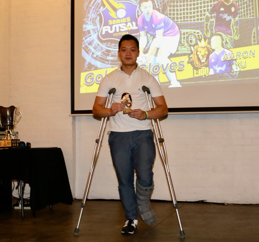 Aaron Yu receives his fourth Series Futsal Victoria Golden Gloves award in crutches but with a smile.