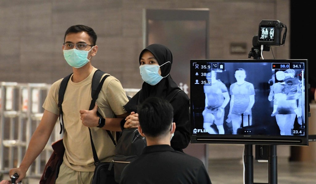 A couple wearing protective face masks amid fears about the spread of Covid-19 walk past a temperature screening checkpoint at Singapore’s Changi International Airport. Photo: AFP