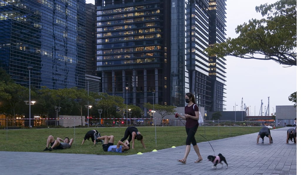 A pedestrian walking a dog passes a group of people work out in a field at the Marina Bay financial district in Singapore. Photo: Bloomberg