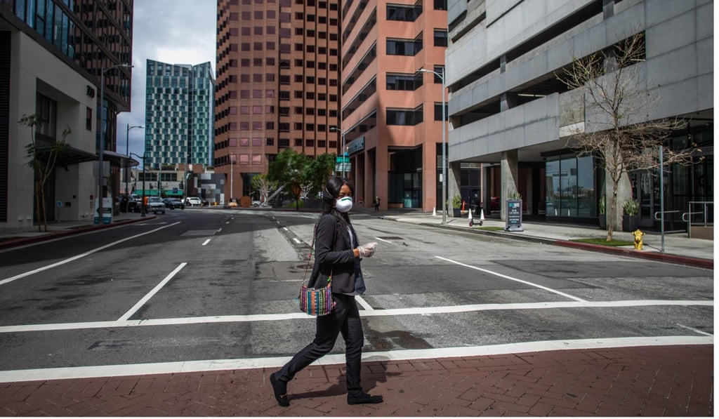 A woman wearing a face mask crosses an empty street in Los Angeles, California. Photo: AFP