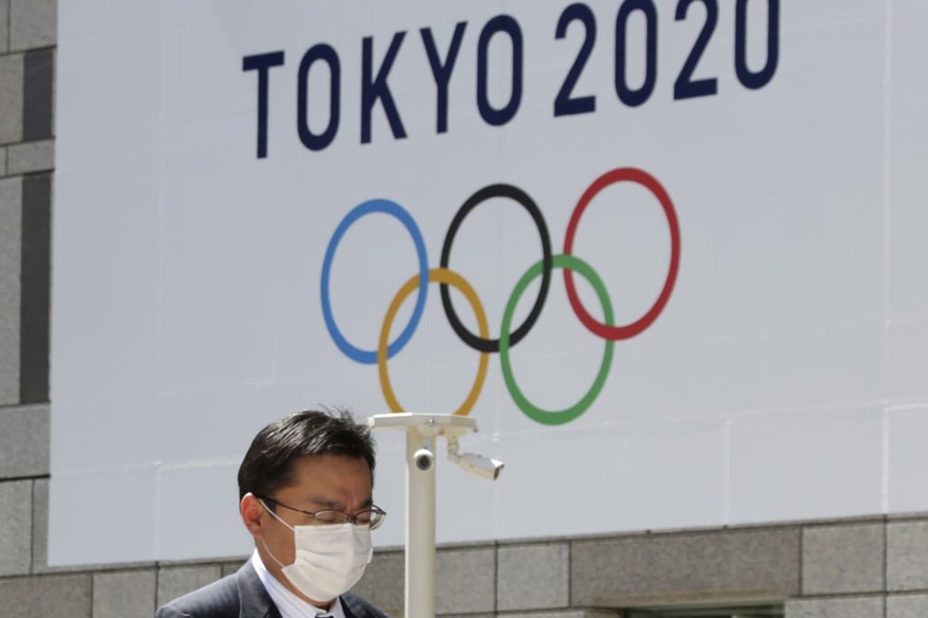 A masked man walks in front of a Tokyo Olympics logo at the Tokyo metropolitan government headquarters building in Tokyo on March 25, 2020. Photo: AP A masked man walks in front of a Tokyo Olympics logo at the Tokyo metropolitan government headquarters building in Tokyo on March 25, 2020. Photo: AP