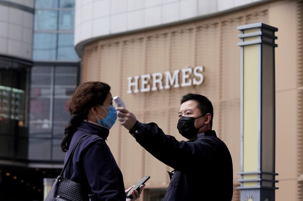 Management staff checks the temperature of a woman entering a shopping centre in Wuhan on March 30. Photo: Reuters