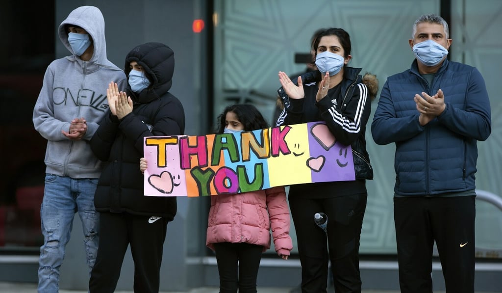 A family holds a sign and applauds health care workers outside St Paul's Hospital in Vancouver, British Columbia, on Sunday. Photo: AP A family holds a sign and applauds health care workers outside St Paul's Hospital in Vancouver, British Columbia, on Sunday. Photo: AP