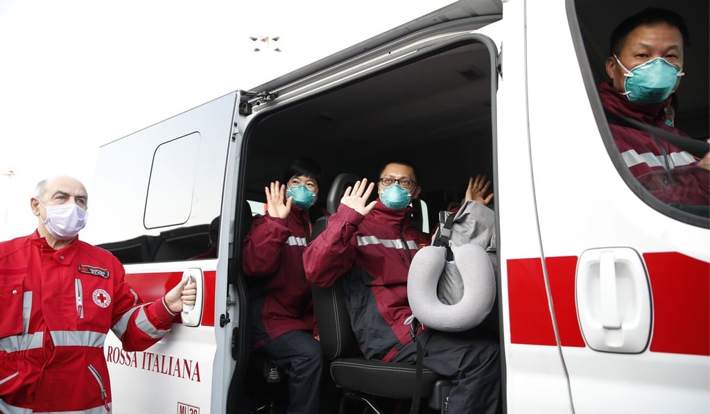 Doctors and paramedics from China wave from a Red Cross vehicle upon arrival at the Malpensa airport in Milan on March 18. China sent over 35 doctors and paramedics and around 20 tons of equipment to the area of Italy most affected by Covid-19. Photo: AP