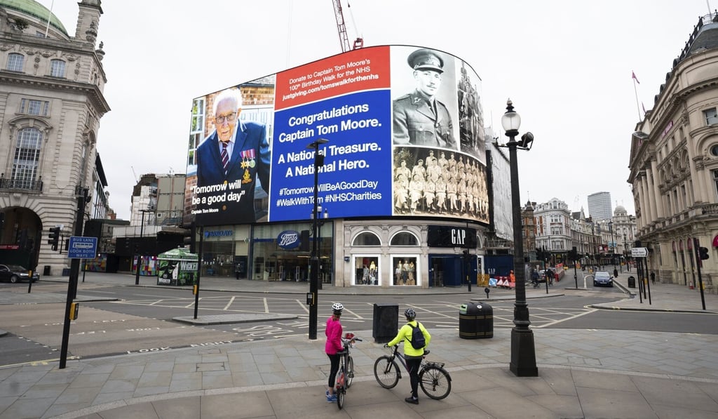 Cyclists look at a hoarding honouring Captain Tom Moore, the army veteran who has raised millions for the NHS, in Piccadilly Circus, London. Photo: AP