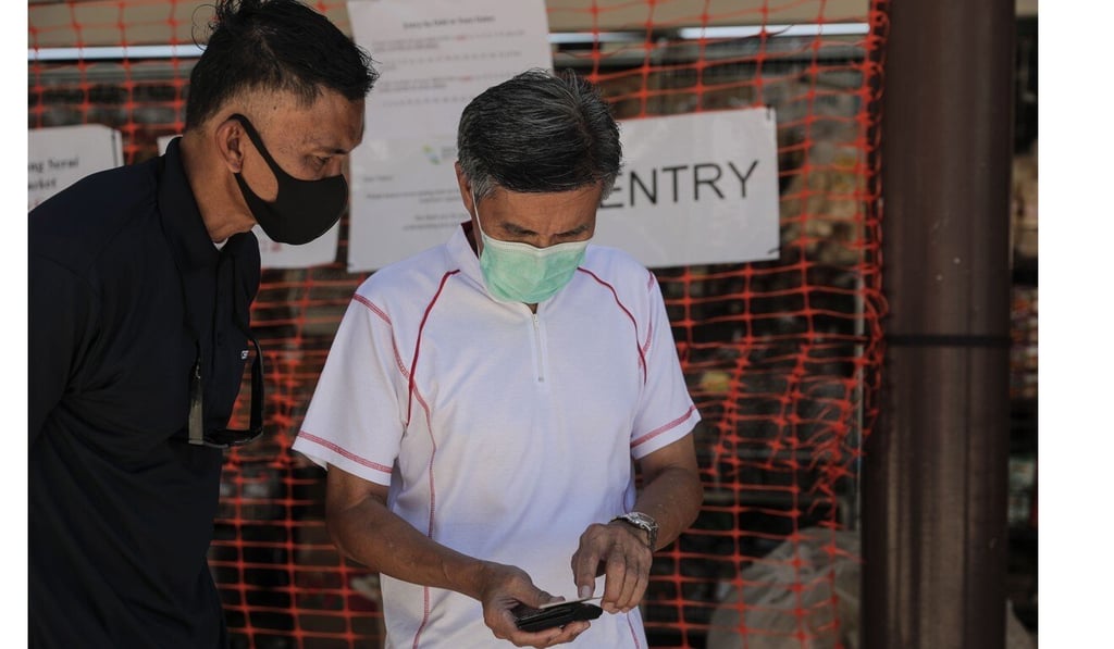 A man has his identity card checked by a safe distancing ambassador before entering a market. Companies in Singapore have redeployed staff to assist with measures to curb the coronavirus outbreak. Photo: EPA-EFE