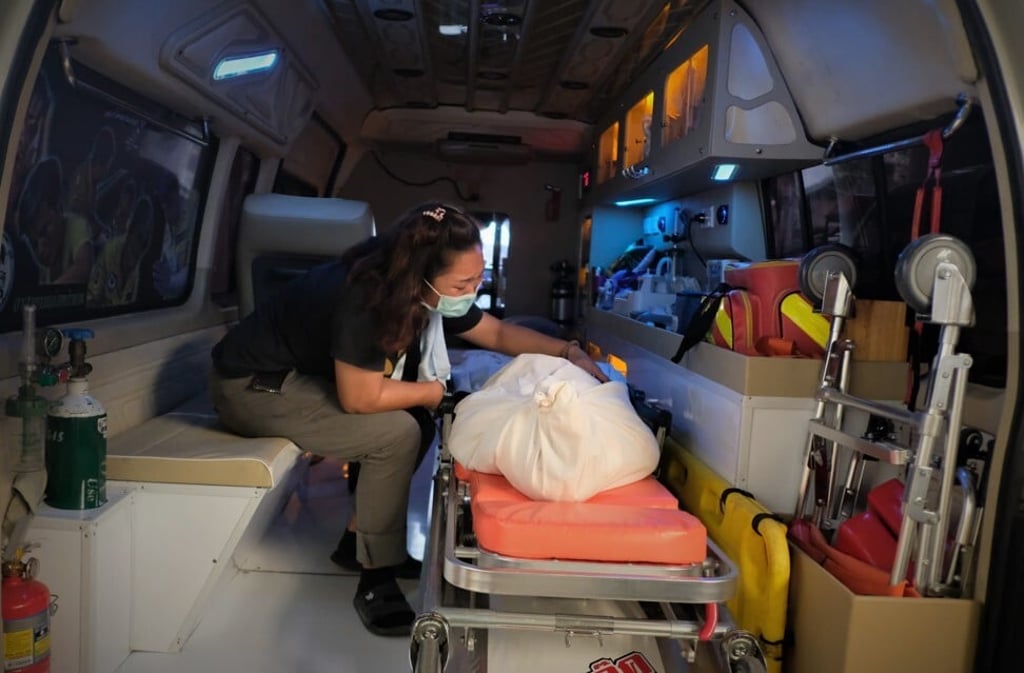 Mullika Junduang strokes the body bag that contains her son in the back of volunteer rescuer Boonyee’s ambulance. Photo: Tibor Krausz